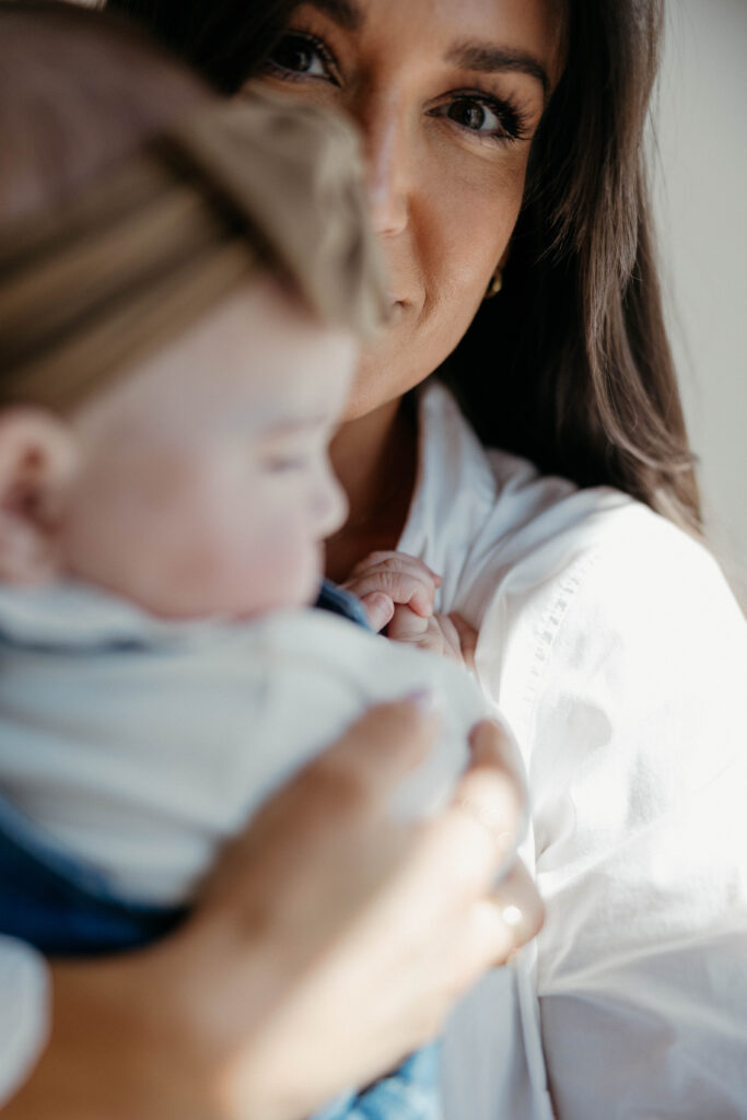mother peeking out looking at the camera with soft smile behind off focus baby during a studio photoshoot with soft natural lighting