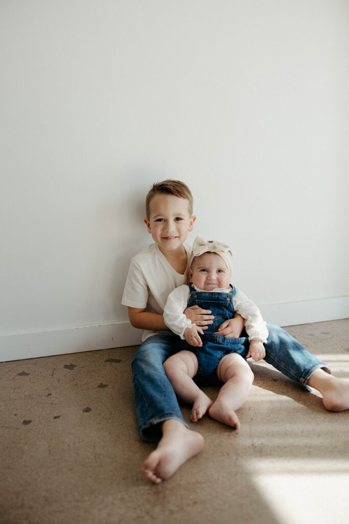 brother and baby sister smiling together during a studio photoshoot with soft natural lighting