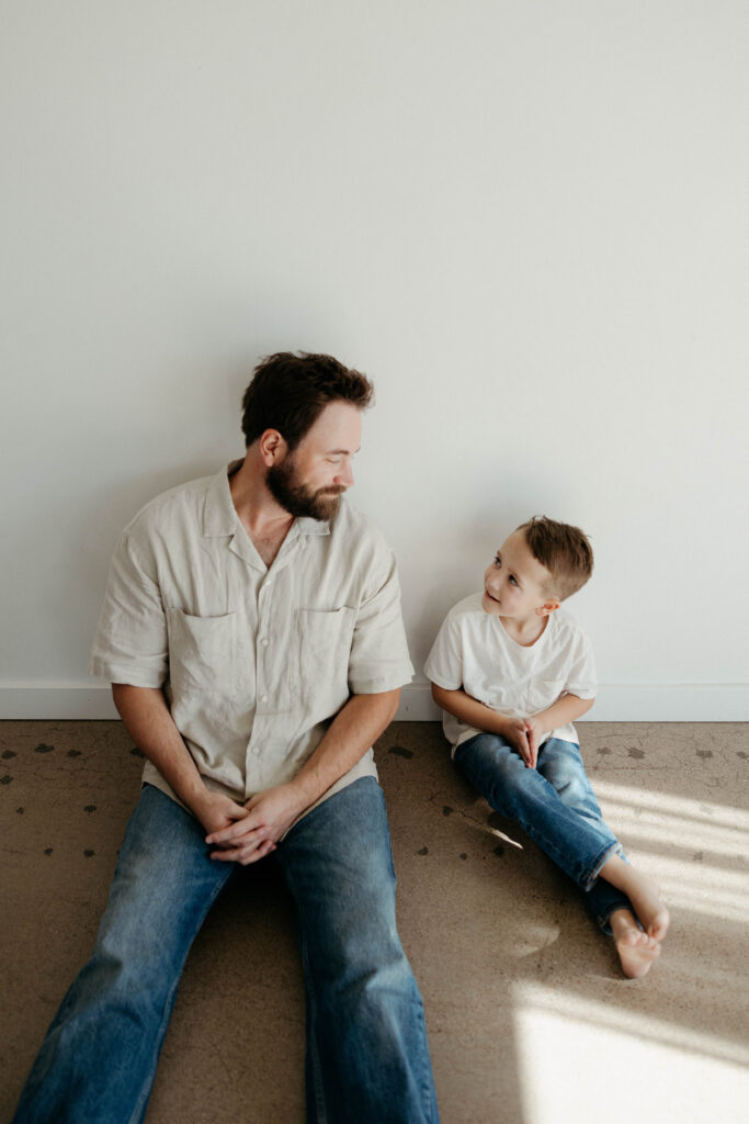 father and son smiling at each other during a studio photoshoot with soft natural lighting
