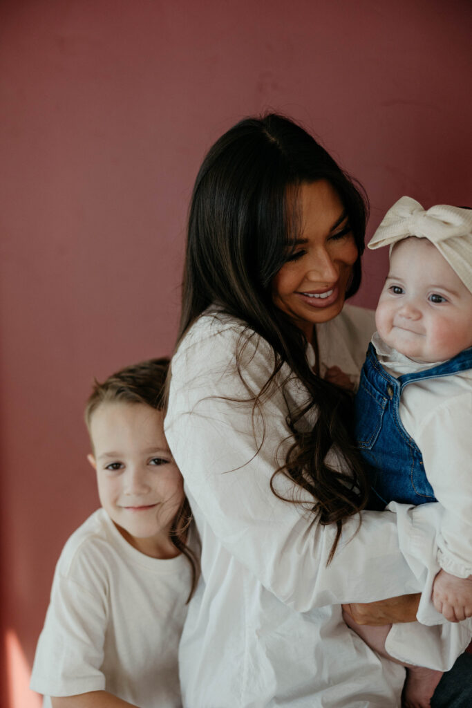 mother and children smiling and snuggling together in portrait with neutral backdrop and soft, even lighting