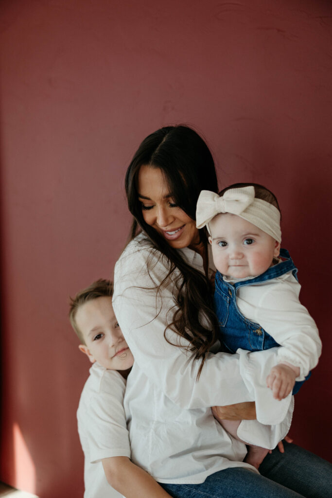 mother and children smiling and snuggling together in portrait with neutral backdrop and soft, even lighting