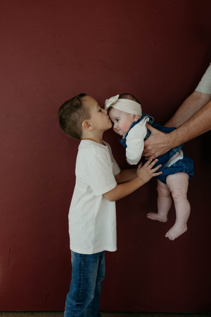 older brother kissing baby sister's forehead during a studio photoshoot with soft natural lighting