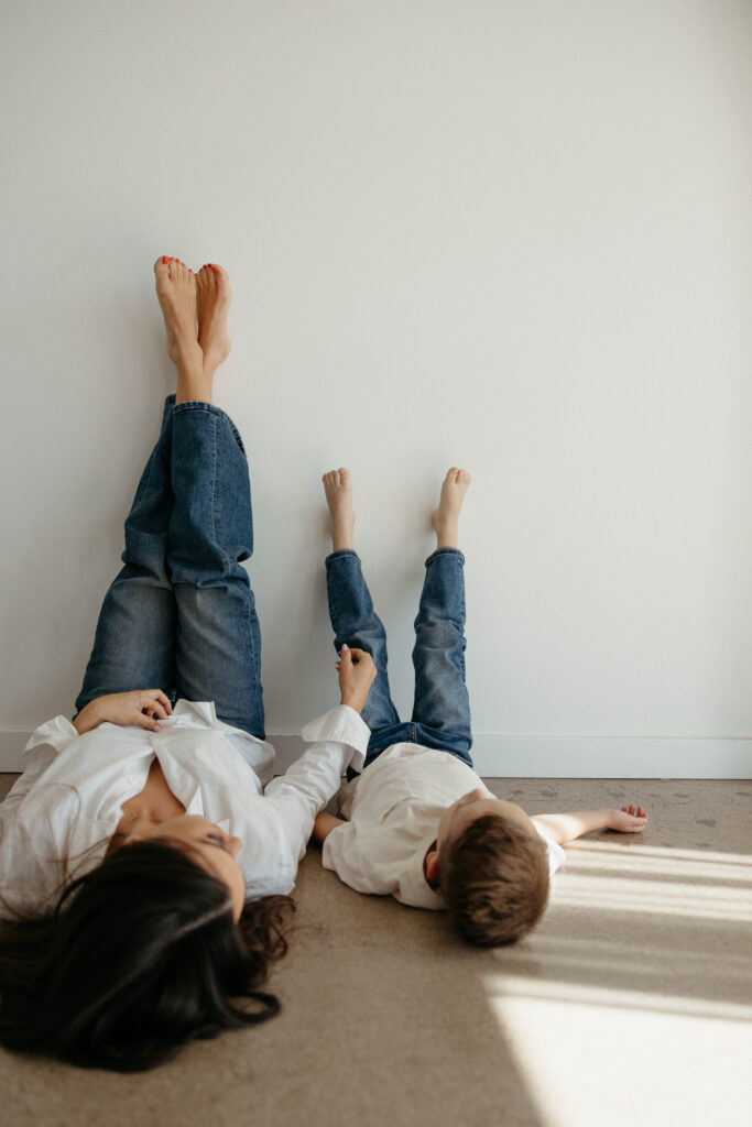 mother and son sitting together with legs up on the wall during a studio photoshoot with soft natural lighting